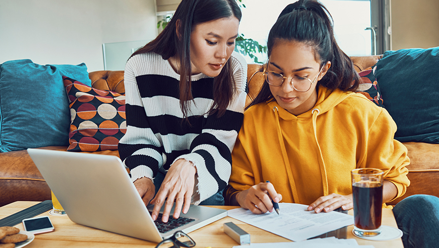 Two friends sitting on a couch studying with a laptop